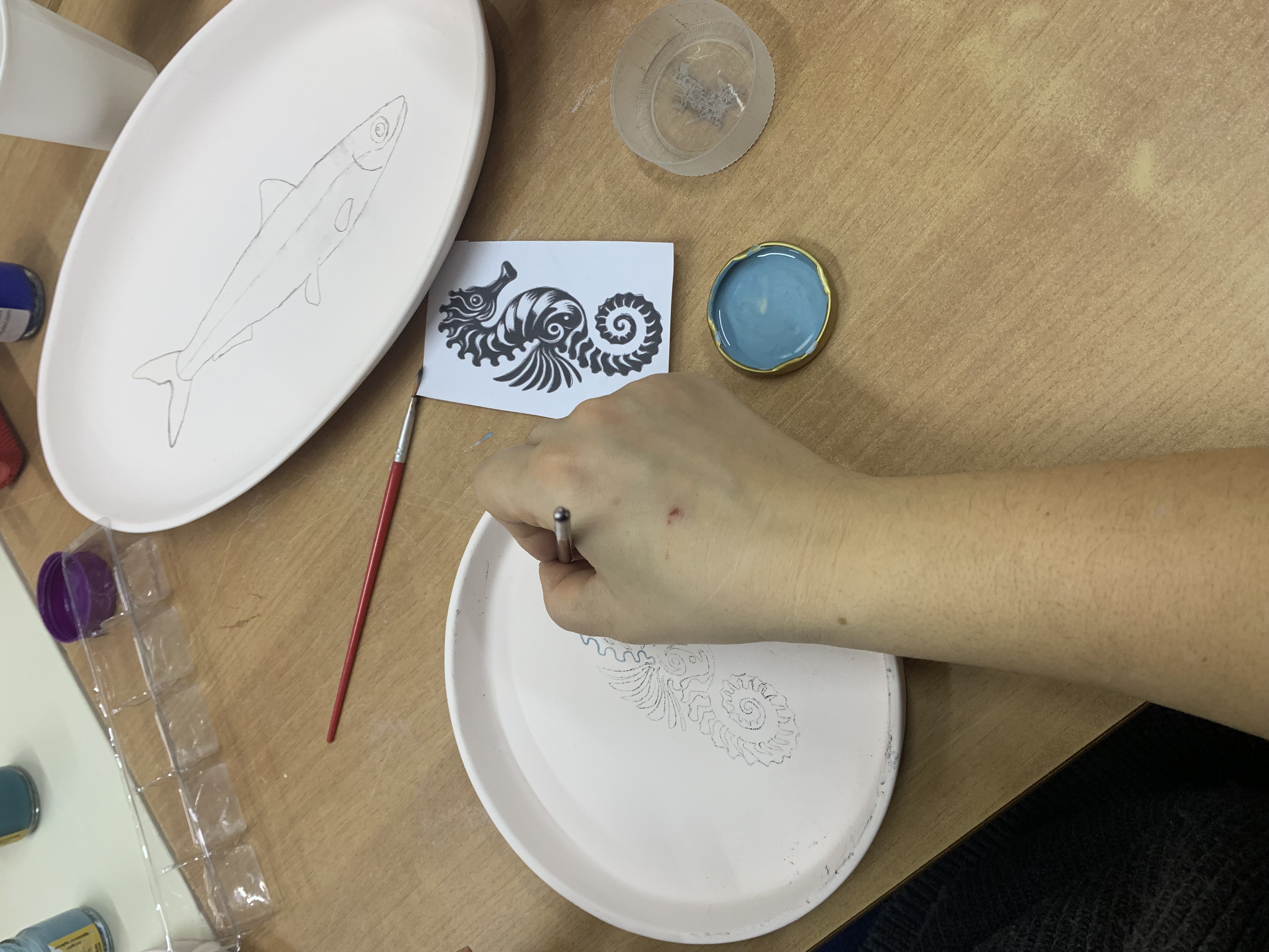 Seramik tabak üzerinde denizatı deseni çizen el.